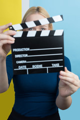 Young woman holding a clapperboard over colorful backgound