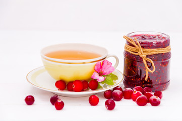 Strawberry jam in a jar with cranberries and a cup of tea