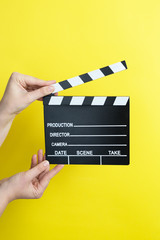 woman holding movie clapper on yellow background, cinema concept