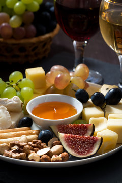 Plate with deli snacks and wine on a dark background, closeup 