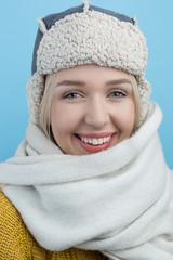 happy young woman in a woolly winter hat with earflaps against b