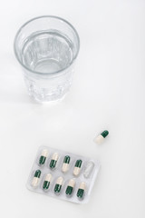 Drugs and pills with glass of water on white background