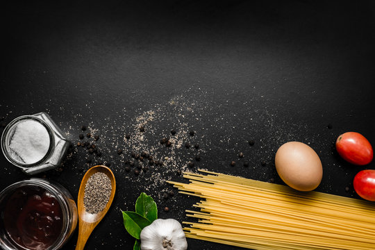 Food frame. Pasta ingredients - tomatoes, garlic,  herbs, salt, spaghetti pasta and egg on  black grunge background with copy space, Top view