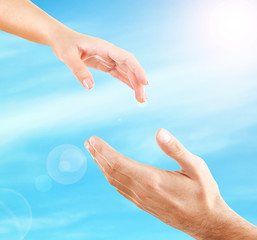 Female and male hands reaching to each other on sky background. Help and care concept.