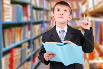Cute little boy with book on blurred school library background.