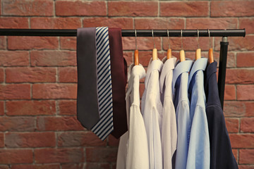 Hangers with male shirts and ties on clothes rail against brick wall background