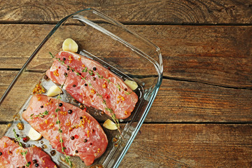 Steaks in marinade with thyme and garlic in glass bowl and wooden background