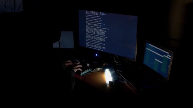 Hacker in hood cracking code using computers in dark room