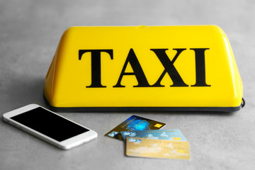 Yellow taxi roof sign with phone and credit cards on gray background, closeup