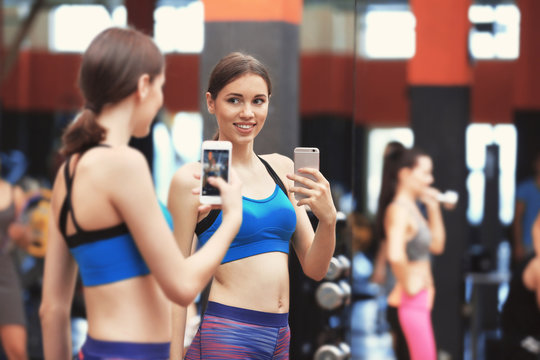Young sportive woman taking selfie near mirror in gym