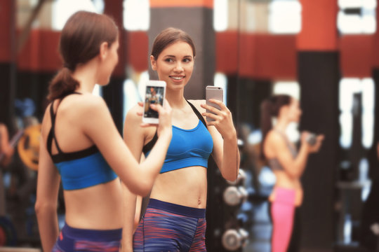 Young sportive woman taking selfie near mirror in gym