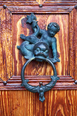 Antique door knock of verdigrised brass, attached to a door of lacquered wood, shaped as a fat child holding a fish kind animal