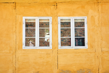Two white colonial style windows in a yellow painted timbered house, in Elsinore, Denmark