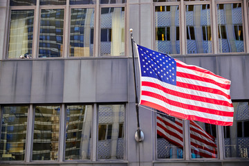 Fototapeta premium The american flag hanging from a pole attached to the facade of a glass and steel skyscraper in New York City