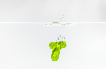 Green wooden alphabet T drop in the water with white background and selective focus