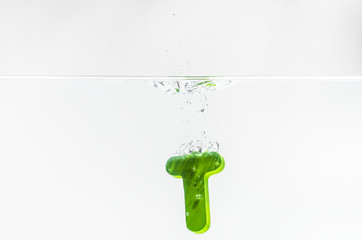 Green wooden alphabet T drop in the water with white background and selective focus