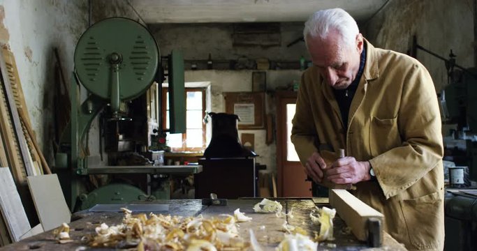 in an old carpentry an elder is working the wood to create a toy airplane with traditional instruments