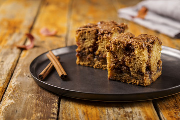 Cinnamon zucchini coffee cake on a black plate on a worn wooden light background with red dry leaves. Selective focus 