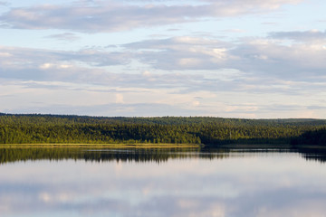 Russia. Karelia. Chupa. Bay of the White Sea. Landscape. Pine forest on the shore. Reflection in water. Cumulus clouds.