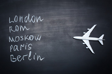 Traveling concept. Toy plane over chalkboard with cities written on it