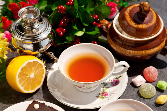 Самовар, чашка чая, лимон, сахар и конфеты под солнечными лучами. Чай с лимоном это классическое сочетание. Чай на фоне цветов смотрится ярко и аппетитно.