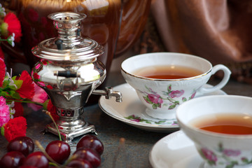 Вишневый чай в двух чайных парах. Самовар с чаем создает домашний уют. Чайный сервиз смотрится изящно.