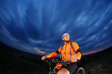 Man in helmet stay on bicycle under sky with clouds.