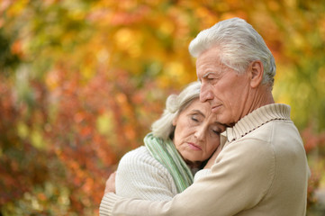 Sad elderly couple standing embracing outdoors