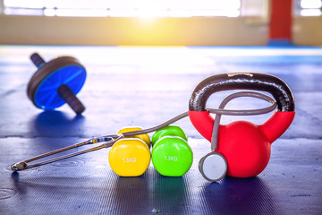 Colorful Dumbbell with stethoscope in gym on blue floor rubber