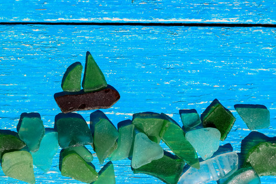 Figure sailboat from multicolored broken glass on blue wooden background