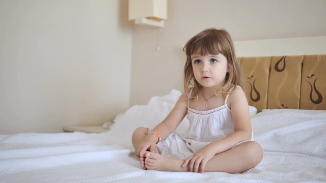 Adorable child in white dress watching tv on the bed