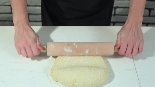 female hands taking rolling pin for making dough on board