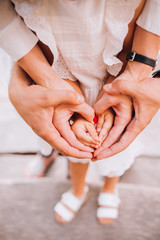 A family of hands form a heart - father on the outside, then mother's hands and infant baby hands in the middle.