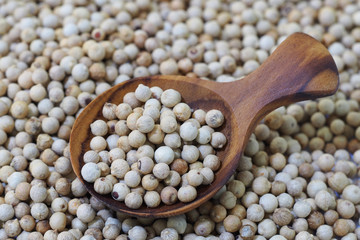 white pepper seeds in wooden spoon on wooden background