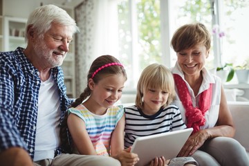 Grandchildren using digital tablet with their grandparents