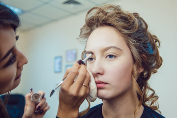 Make up artist doing professional eye makeup of young woman near the mirror in beauty studio