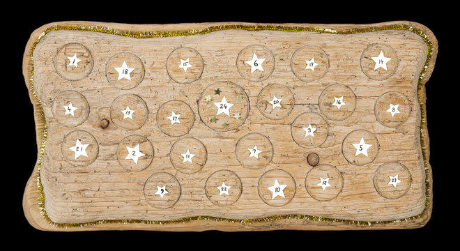 Advent calendar handmade from old timber with circular spaces for small items. Special calendar to count twenty four days before Christmas. Medieval wood with wormholes. Photo from above over black.