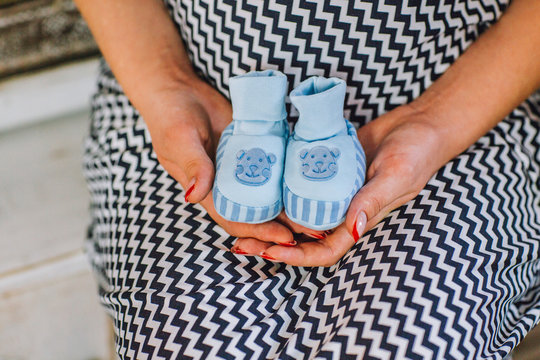 Pregnant woman holding baby booties for newborn boy, girl with blue baby shoes expecting boy, pregnancy concept, Newborn baby booties, selective soft focus,  closeup