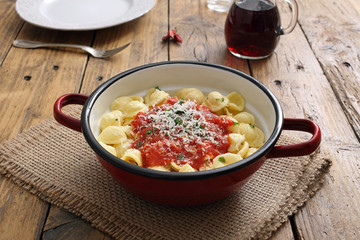 pasta italiana orecchiette con pomodoro e formaggio in tegame di metallo sfondo legno rustico