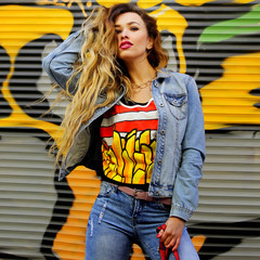 Beautiful fashionable woman in denim clothes standing against graffiti wall.