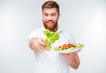 Smiling man showing green lettuce and plate with fresh salad