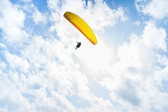 Yellow paraplane in the blue sky with clouds.