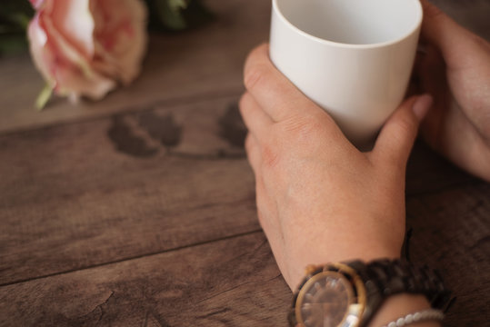 Girl is holding white cup in hands. White mug for woman, gift. Female hands with watch and bracelets holding hot cup of coffee or tea in mor