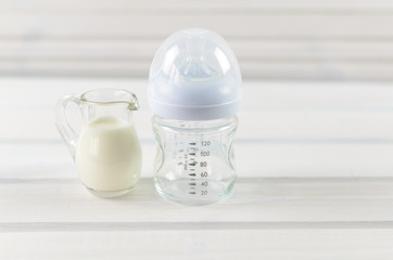 Fototapeta na wymiar Glass baby bottle and milk jug on white wooden background