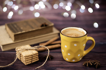 Mug of coffee, cookies, star anise, cinnamon, old books. Blurred lights, wooden background. Winter time, Rustic background with beautiful Christmas lights of bokeh.