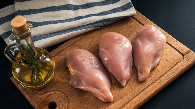 Raw chicken breasts and spices on wooden cutting board