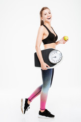 Happy fitness woman holding weighing machine and green apple
