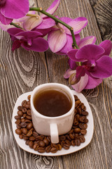 Small white cup of coffee, roasted coffee beans, orchid on wooden background