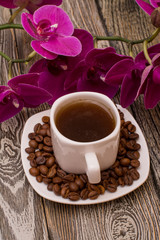 Small white cup of coffee, roasted coffee beans, orchid on wooden background