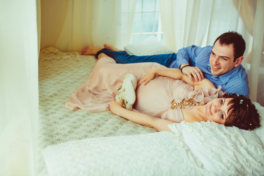 Dreamy expecting couple enjoys a moment while resting on the bed